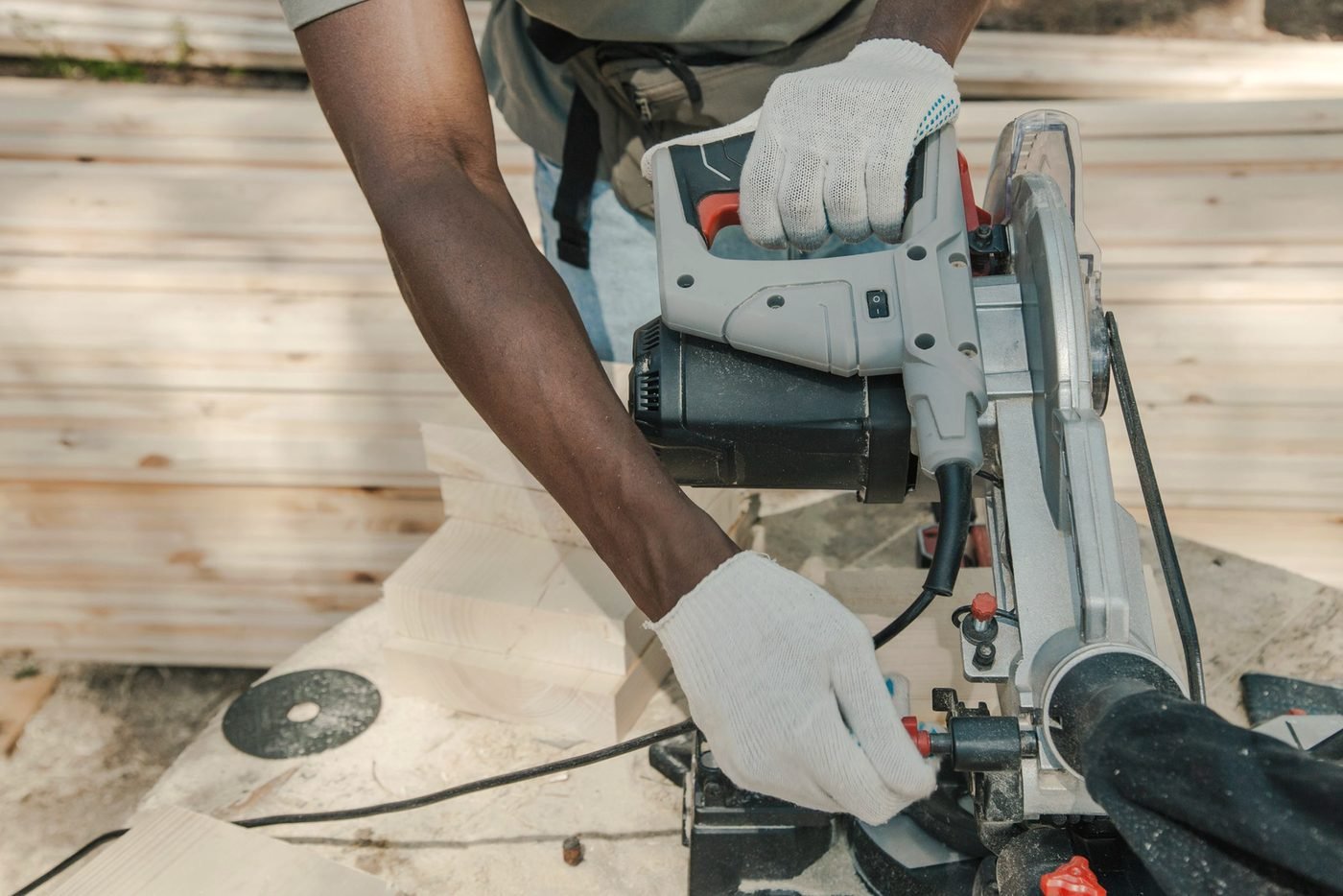 Gloved hands guiding a miter saw through a board.